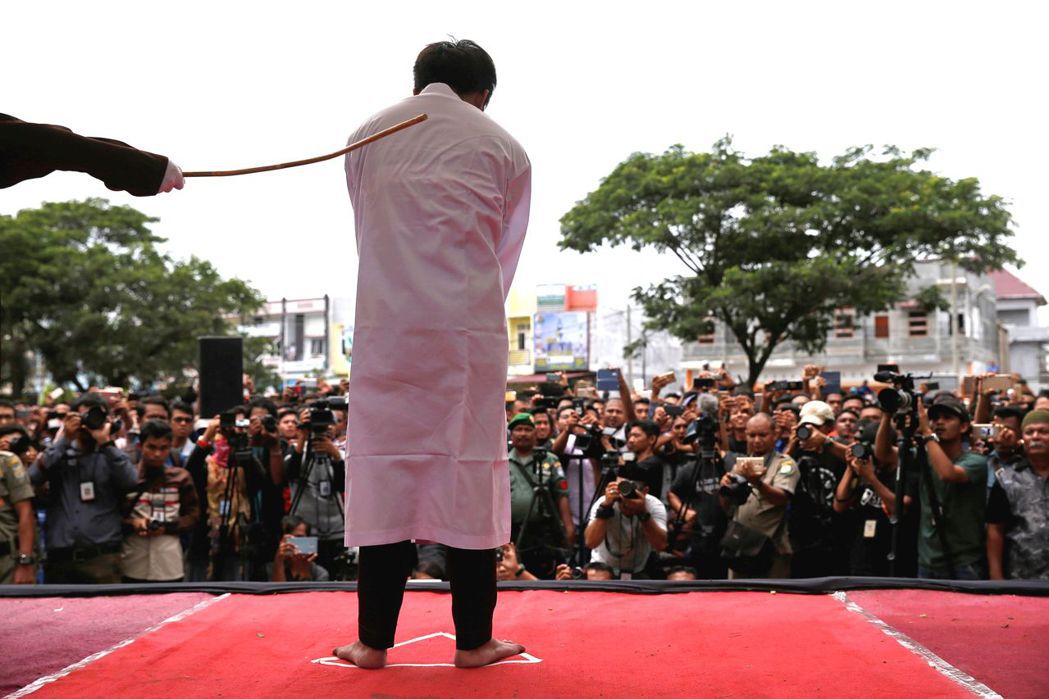 印尼同志青年違反伊斯蘭律法，於23日遭鞭刑示眾，台下有許多人拿手機拍攝行刑。 （...