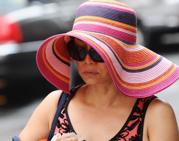 一婦女戴著墨鏡與大涼帽在烈日下走過華埠街頭。記者簡一夫／攝影