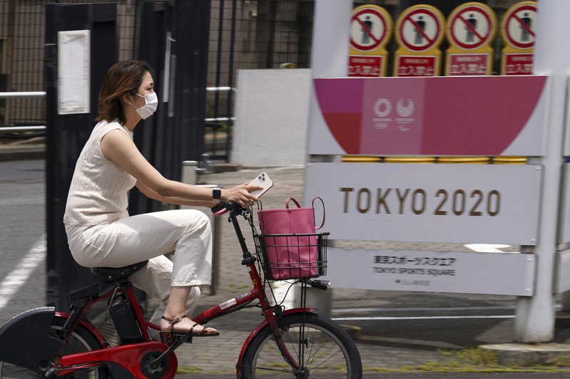 东京疫情烧 东京街头一名女子廿六日戴口罩骑车经过东奥与帕奥的宣传旗帜。（美联社）(photo:UDN)