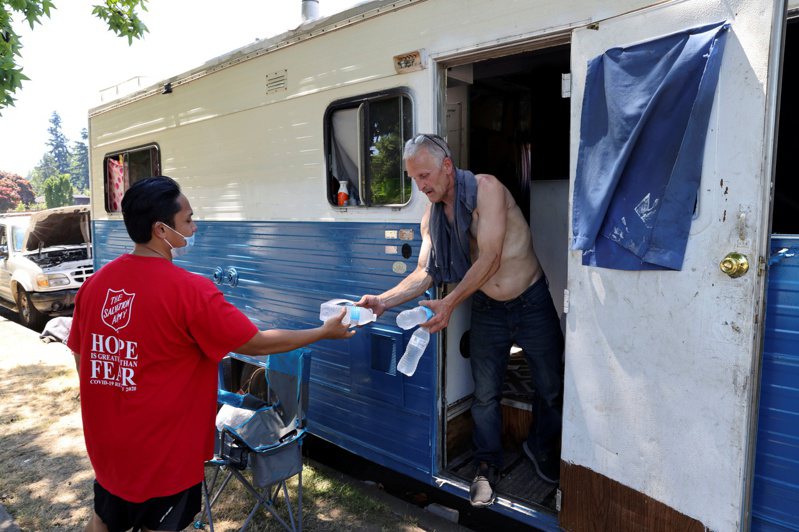 美國西雅圖上月廿七日遭熱浪侵襲，一名志工（左）拿包裝水給住在露營車的男子，並請他到附近的消暑中心避暑。（路透）