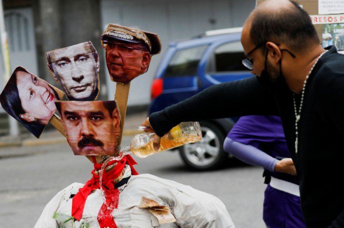 委内瑞拉庆祝复活节，一名男子在挂有委内瑞拉总统马杜洛、俄罗斯总统普亭与另2名政治人物照片的人偶淋上汽油。路透(photo:UDN)