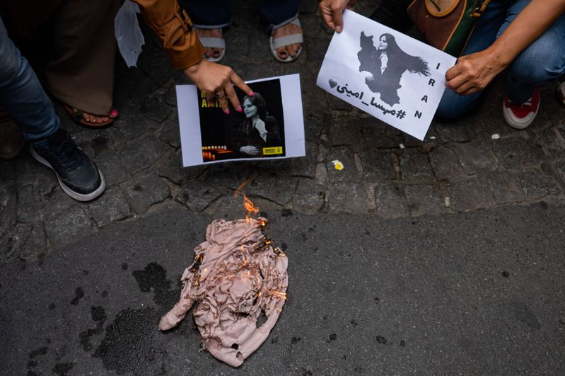 抗议民众21日在土耳其伊斯坦堡的伊朗领事馆外焚烧头巾抗议，一旁有人手持据信为死者玛莎的照片。（法新社）(photo:UDN)