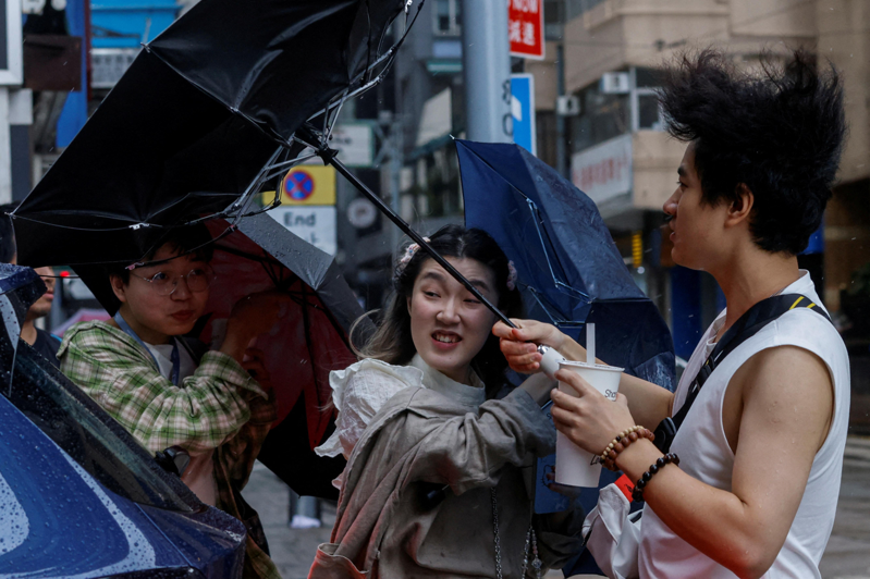 受小犬颱風影響，港股9日上午暫停交易。圖為8日香港街頭景象，強風將民眾的雨傘吹到開花。路透