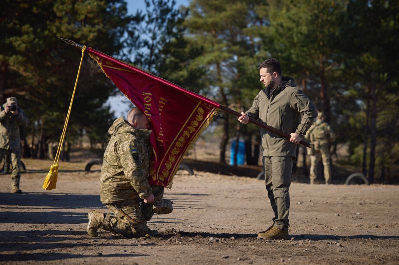 近日烏克蘭內部文武不睦浮上檯面。圖為烏克蘭總統澤倫斯基（右）三日訪視烏國境內一處訓練中心時，將一面戰旗頒給一個軍方單位。（法新社）