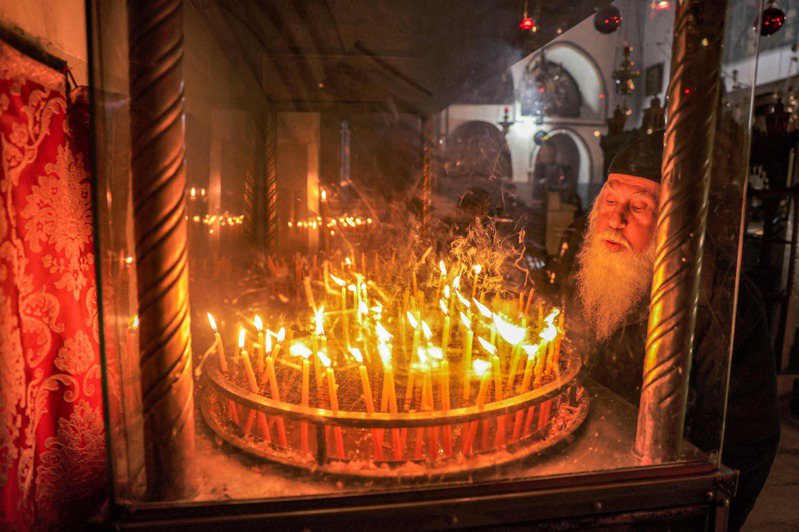 巴勒斯坦基督徒昨天在伯利恆嚴肅舉行耶誕節前的守夜活動，他們點燃燭光詠唱讚美詩，並為加薩祈禱和平。圖為一名基督教信徒在被佔領的約旦河西岸聖經城市伯利恆聖誕教堂的聖像前點燃蠟燭。法新社