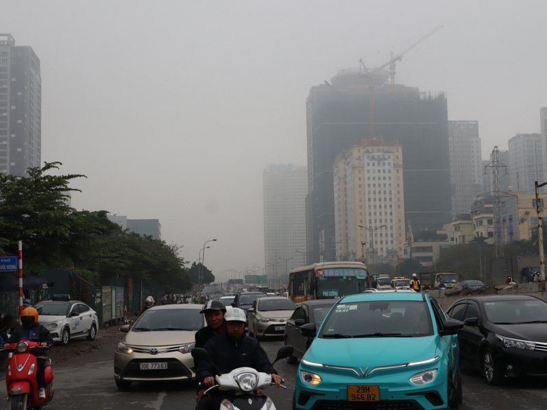 越南首都河內市共有650多萬輛摩托車，被視為主要的空氣汙染源之一。圖攝於4日上午10時22分，汽機車駕駛們背後的天空一片灰濛濛，當時空氣品質指標（AQI）逼近「非常不健康」程度。中央社