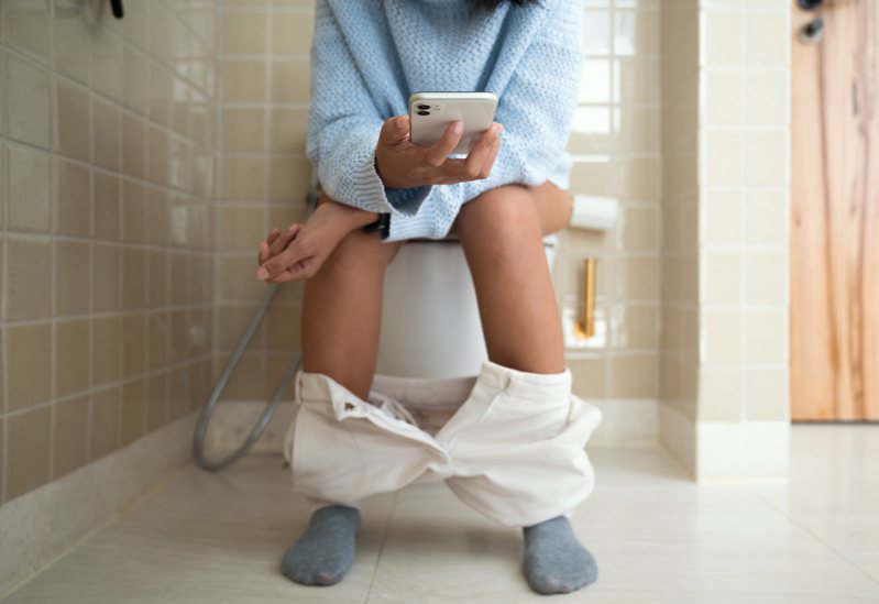醫師建議最好不要帶手機如廁，若是如此做了應該做好手機清潔，以免細菌藏在手機上成為潛在感染源。此為帶手機如廁示意圖。圖／Ingimage