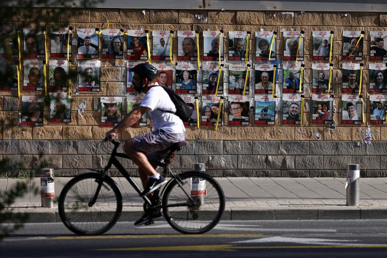 民众6日骑单车经过以色列特拉维夫一幅挂有一批被哈玛斯掳走人质照片的墙。路透社(photo:UDN)