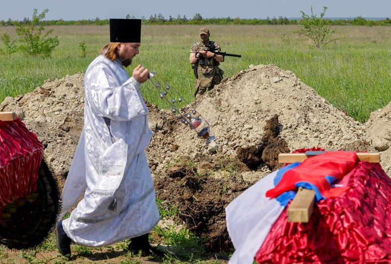 俄占烏克蘭東部盧甘斯克州一處公墓舉行埋葬60名俄軍與3位平民的葬禮，一名牧師走過棺木。攝於2023年5月。BBC報導，俄軍在烏克蘭陣亡的人數現已突破5萬大關。路透