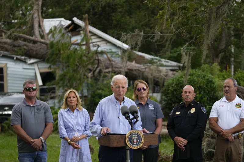 颶風伊達利亞肆虐後，拜登總統(中)2日探訪佛州災區，他身後是傾倒的大樹和損壞的房屋。(美聯社)