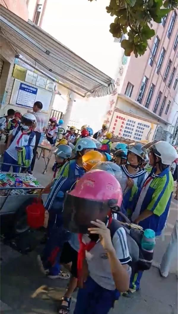 網傳視頻顯示，在角尾鄉中心小學校門口，幾十名學生走路時紛紛戴著頭盔。（取材自央廣網）