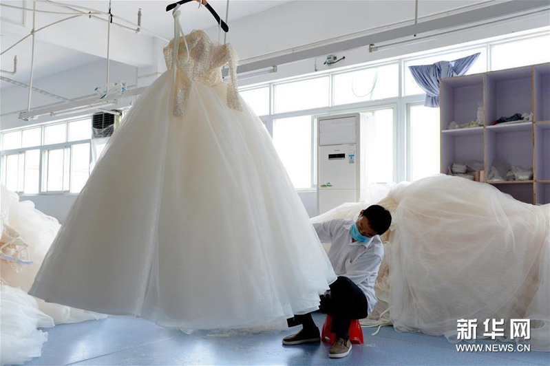工作人員在安徽六安市丁集鎮的一家婚紗生產企業內修剪婚紗的裙擺。（取材自新華網）