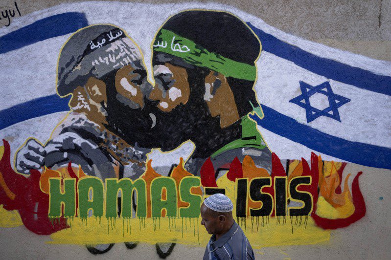 以色列特拉維夫一名男子走過一幅新的塗鴉前，上面畫了哈瑪斯和ISIS成員親吻，並寫著哈瑪斯等於ISIS。(美聯社)