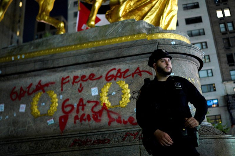 一名纽约市警站在被挺巴示威者涂鸦破坏的中央公园雕像旁。(路透)