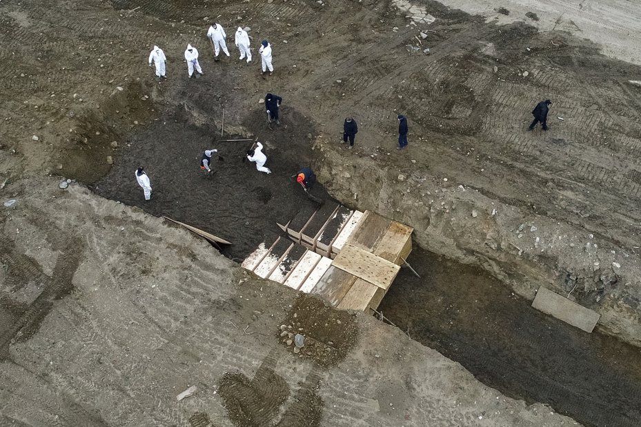 紐約市哈特島的空拍畫面拍到穿防護衣的工作人員挖壕溝集體埋葬幾十具棺木。美聯社
