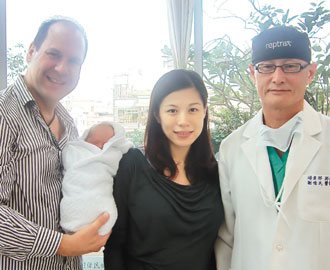 許姓婦女（中）經醫師劉偉民（右）開刀摘下比胎兒還大的子宮肌瘤後，產下健康女嬰，左為德籍丈夫抱著新生女兒。 圖／劉偉民提供