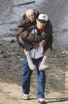 能順利背著家人逃離災難現場，是不幸中的幸福。圖為日本仙台附近的多賀城，年輕人背著老人家撤離家園。 圖美聯社
非報系