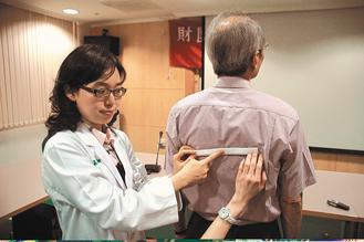 醫師葉怡嘉（左）昨教民眾自我檢測，以直尺放在兩肩胛骨的兩側，如尺斜了就是有長短腳。 記者蔡維斌／攝影