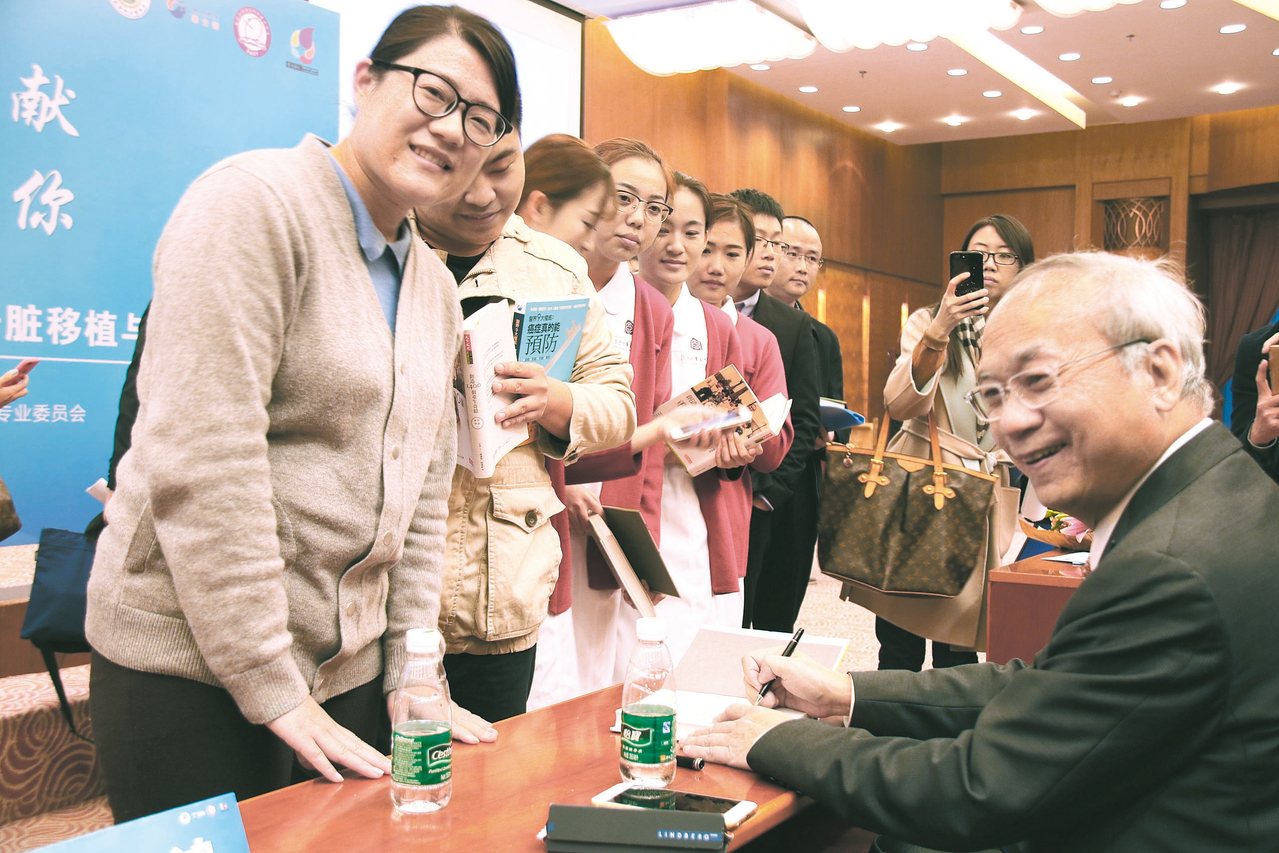 大陸民眾拿著高雄長庚醫院榮譽院長陳肇隆（右）所著、本報出版的「癌症真的能預防」等書，請他簽名。