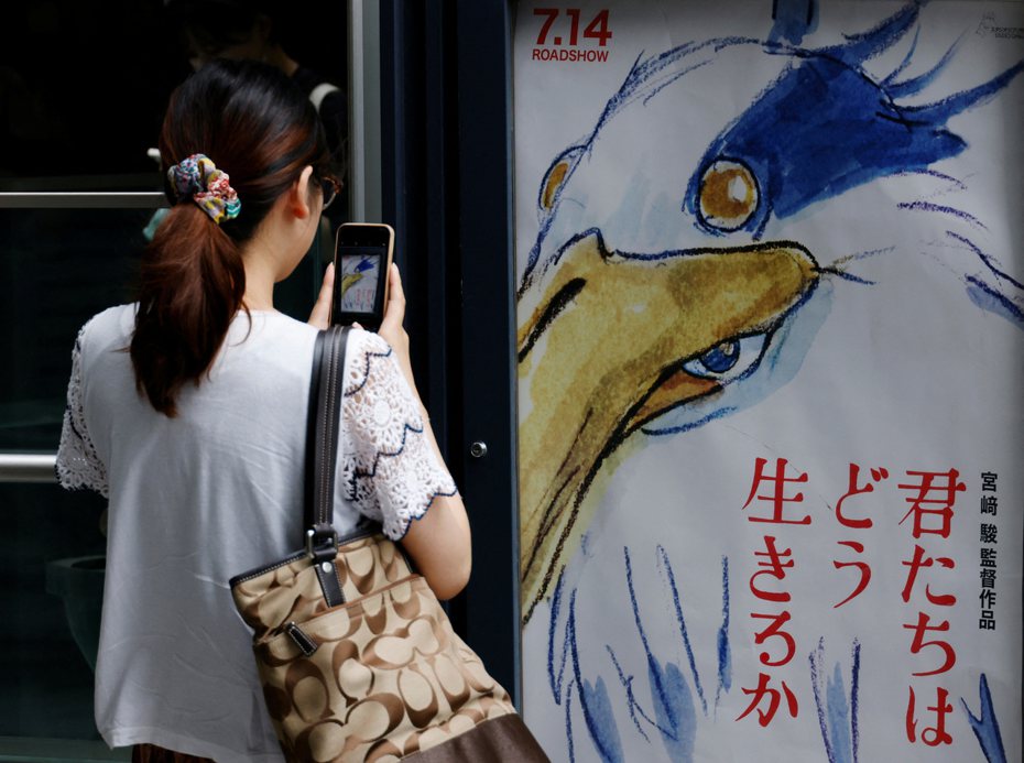 宮崎駿新片「你想活出怎樣的人生」在日本上映，影迷拿手機拍下海報畫面。（路透）