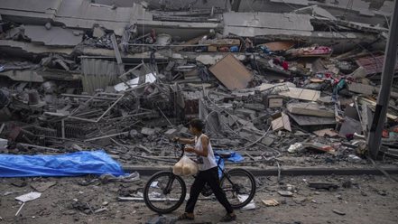一名巴勒斯坦兒童推着自行車走在加沙一棟被以色列軍隊空襲摧毀的建築廢墟前 2023年10月8日 AP - Fatima Shbair