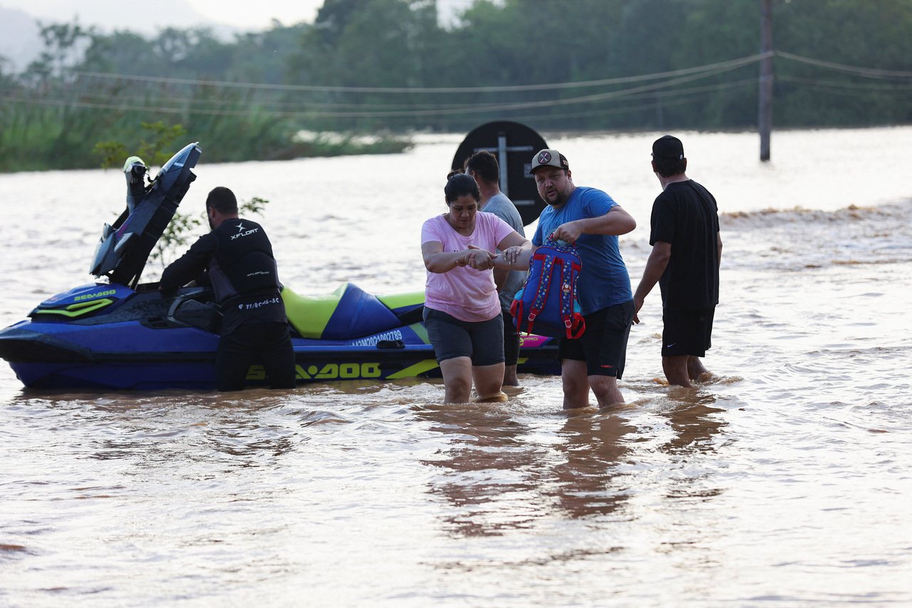 巴西頻繁暴雨造成土石流和洪水，氣象學家預估，11月降雨量已高於平均水準的地區，12月也將發生暴雨；圖為聖卡塔琳娜州居民在淹水區行走。（路透）