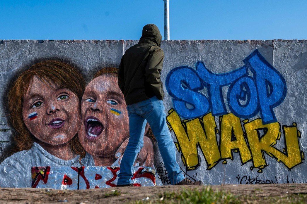 圖為德國柏林一位行人經過一面畫上「停止戰爭」字樣與烏克蘭國旗顏色的牆面塗鴉。 圖／法新社