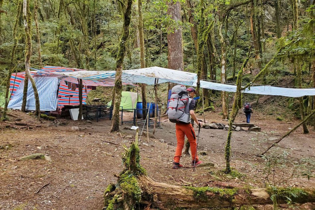 從新武呂溪營地為起點，協作業者以顏色鮮明的藍白和紅藍帆布搭起了規模可觀的遮雨棚、疑似石頭砌成的爐灶和金屬框架。 圖／作者提供