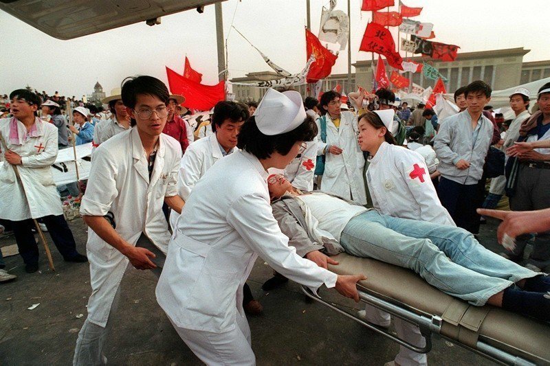 醫護人員正救助一名因絕食而暈倒的學生，攝於1989年5月17日，北京天安門。 圖／法新社