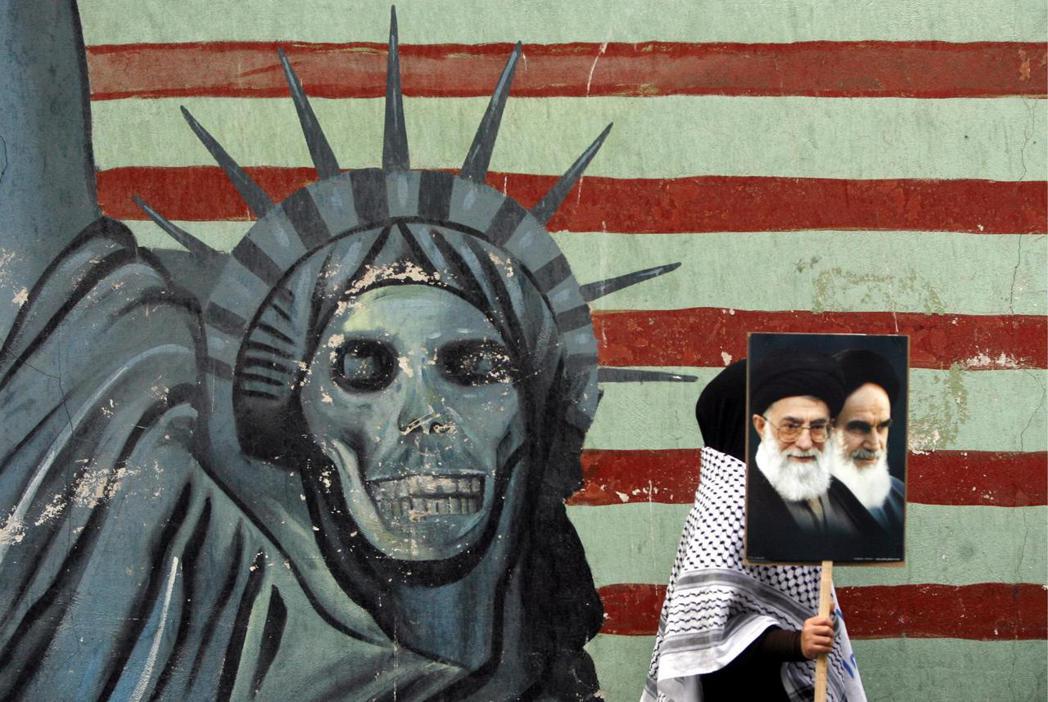 2009年，一名伊朗學生手持何梅尼、以及現任伊朗最高領袖哈米尼照片走過一幅反美壁...