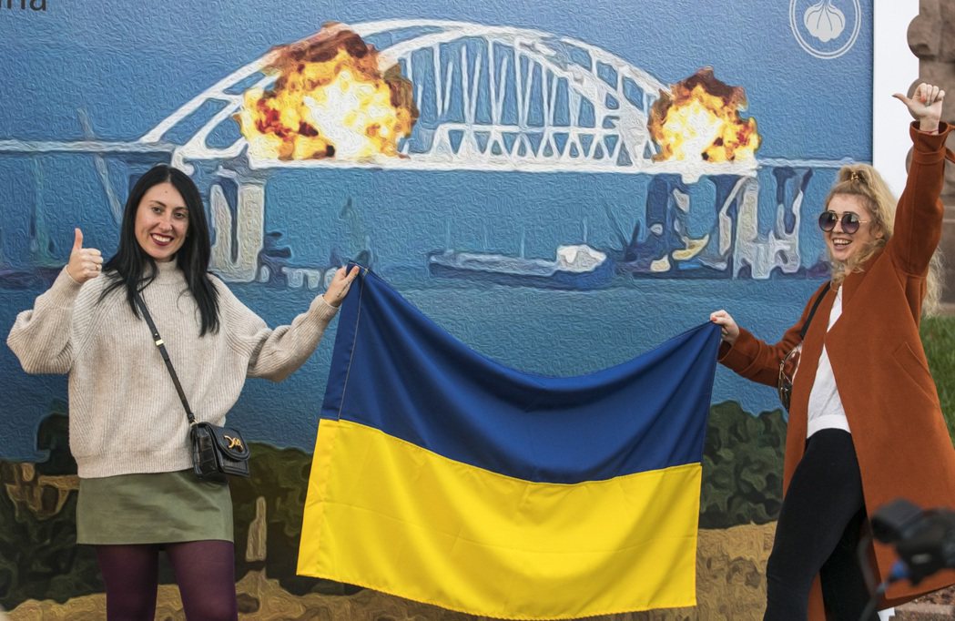 烏克蘭民眾在克里米亞大橋遭炸毀的圖畫前，舉起國旗慶賀。 圖／歐新社