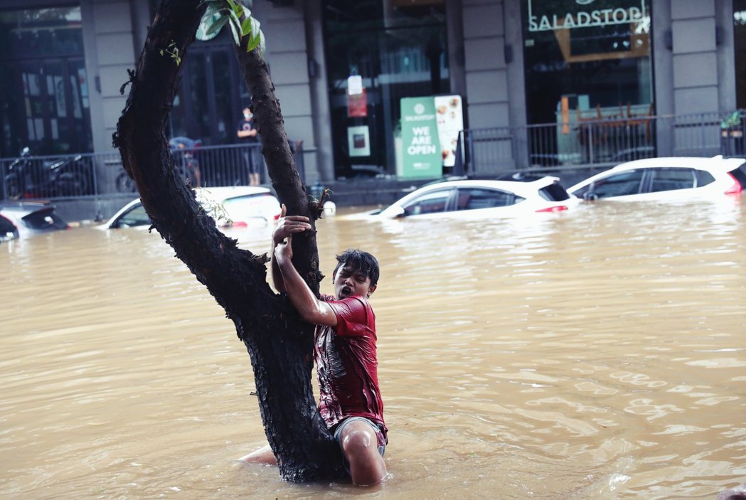2021 年 2 月，淹水的雅加達，一名男生抓著一棵樹以防被洪水沖走。 圖／美聯...