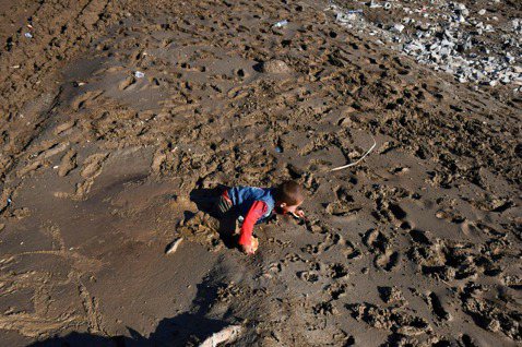 阿富汗10日遭遇豪雨導致的水災，圖為一名幼童在泥濘上艱難爬行。 圖／法新社