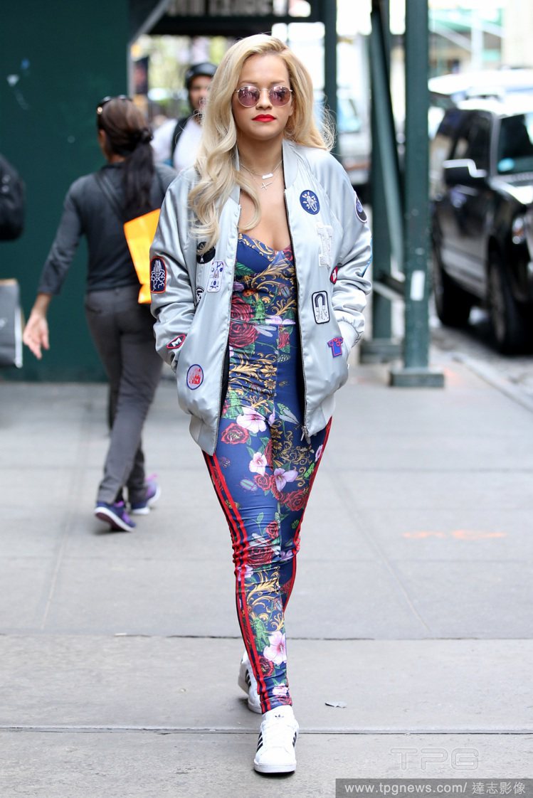英國女星 Rita Ora 平常打扮很潮。她以徽章飛行員夾克，搭配連身印花褲裝與運動鞋，渾身散發街頭潮流味，而彩色墨鏡則為這身運動風造型增添摩登俐落氣息。圖／達志影像