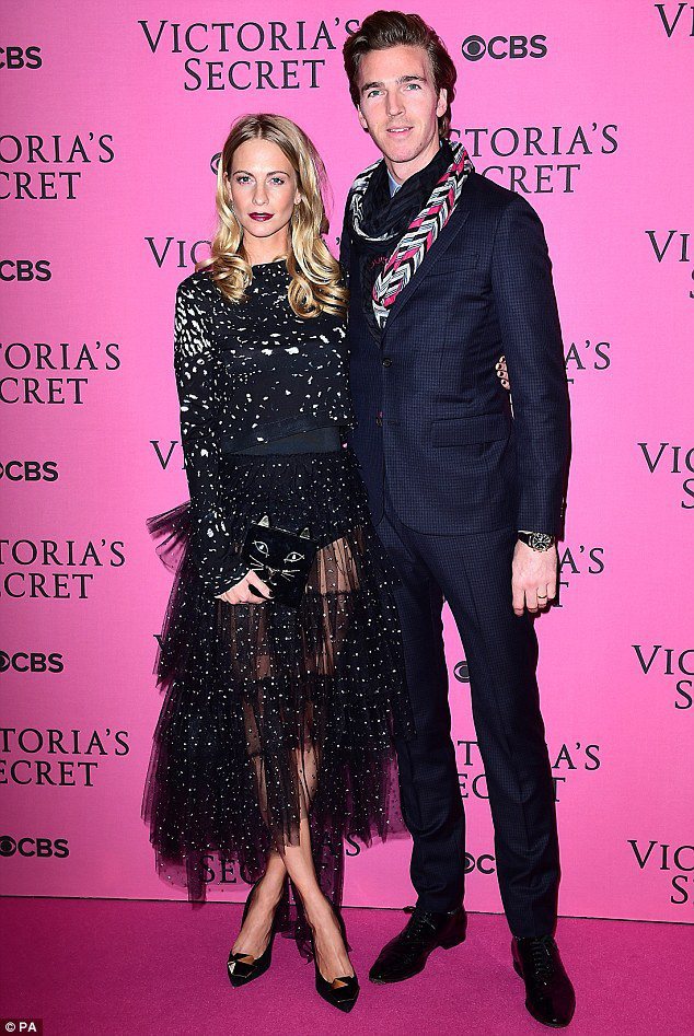 Poppy Delevingne 和老公一起參加 Victoria's Secret 2014 大秀。黑色系的印花上衣搭透膚紗裙既夢幻又性感，很符合活動主題。Charlotte Olympia 的貓臉手拿包則增添搞怪可愛的氣息。圖／擷自英國每日郵報