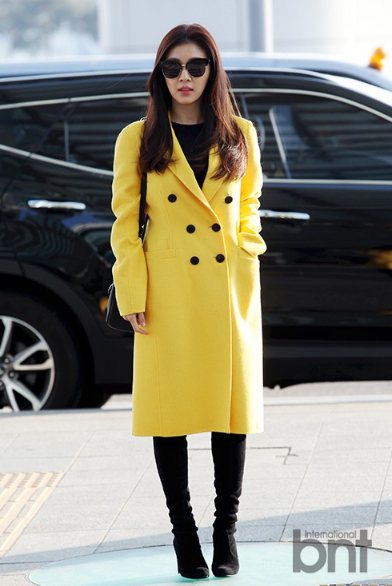 韓國女星河智苑身穿鮮黃色長大衣，搭配黑色高領與高跟長靴，打造時髦優雅的都會風情。圖／BNT提供