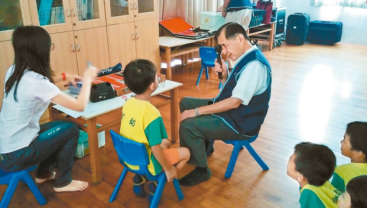 許明木(右)替孩童檢查視力，常透過遊戲或口技與孩童拉近距離。