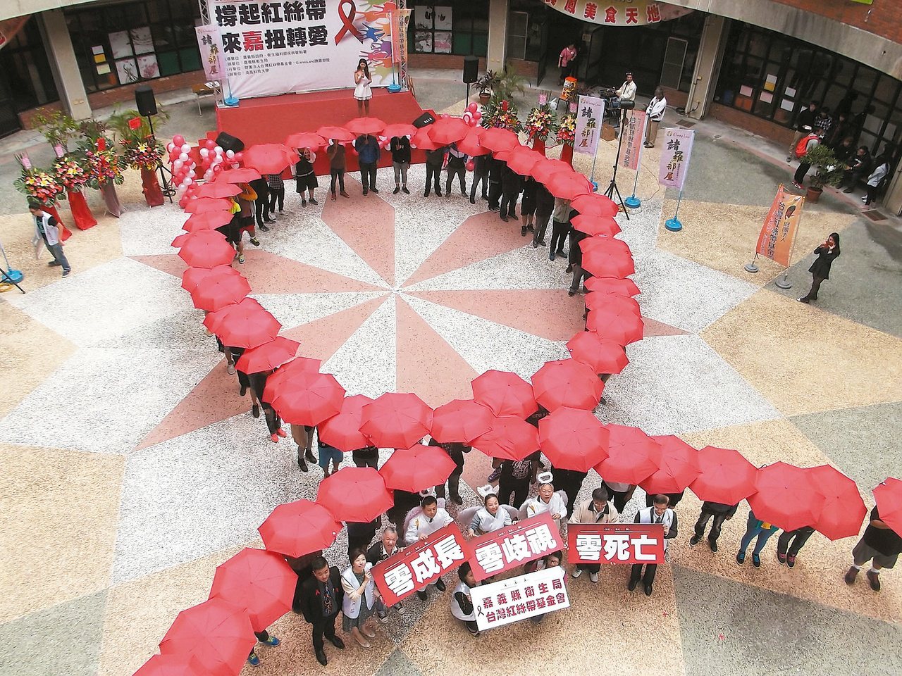 200名學生一同撐起紅色雨傘，排列成象徵關懷愛滋的巨型紅絲帶，期許邁向「愛滋三零」的目標「零成長、零歧視、零死亡」。