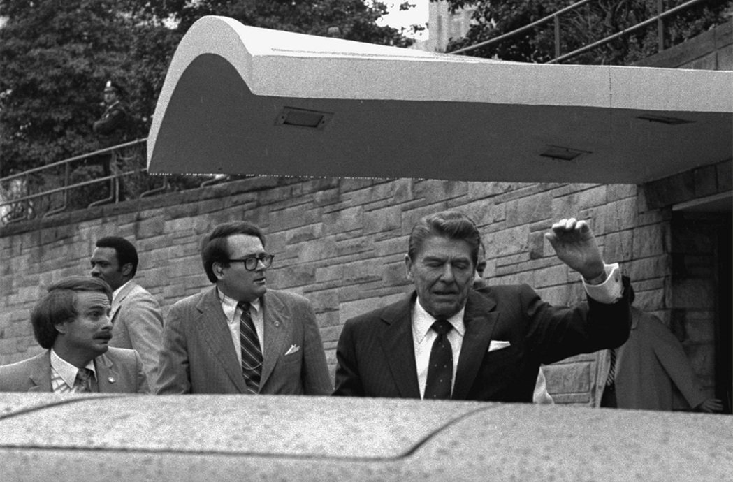 雷根總統1981年3月30日離開華府一家飯店時，被刺客槍傷後，舉起左手。 （美聯...