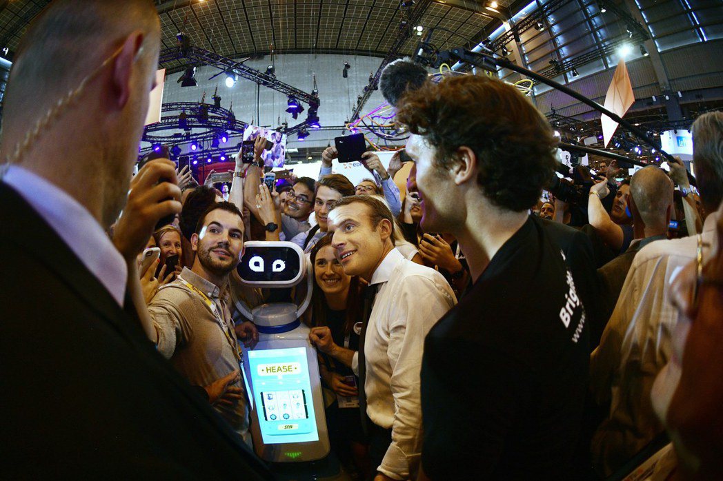 法國總統馬克宏（中）十五日在巴黎參觀科技展，與機器人和民眾自拍。 （歐新社）