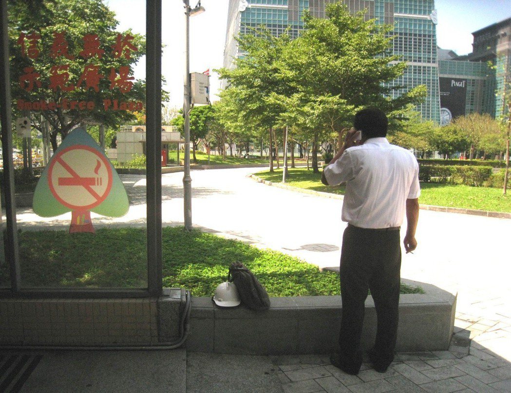 台北市無菸公園常見菸蒂，遭批評政策半吊子；圖為一名男子在信義廣場邊講電話邊吸菸。...