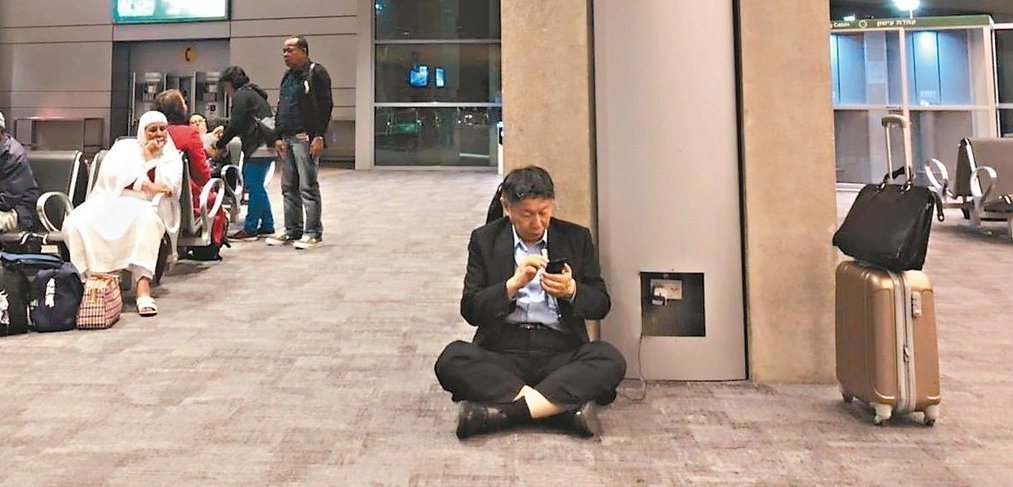 台北市長柯文哲臉書照片，他身穿西裝在國外機場席地而坐，以公用電替手機充電，引發熱...