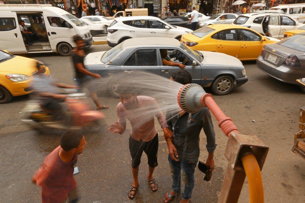 炎炎夏日，許多伊拉克民眾在在街邊沖水消暑。（美聯社）