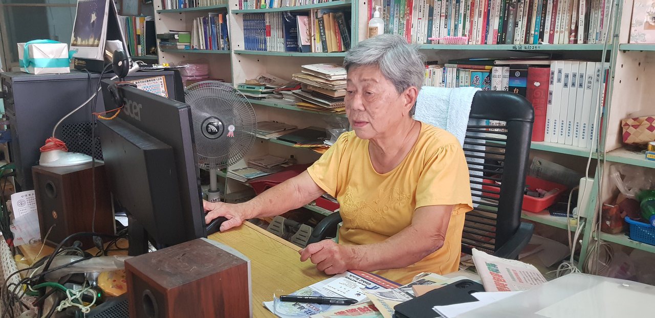 82歲的鄭夙良在自家店面裡打電腦寫作。圖／修瑞瑩攝影