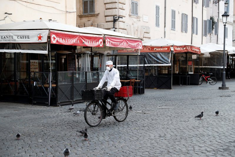 義大利因疫情嚴重，10日起全國封鎖，圖為11日的羅馬市鮮花廣場，一名外送員戴著口罩騎自行車。路透