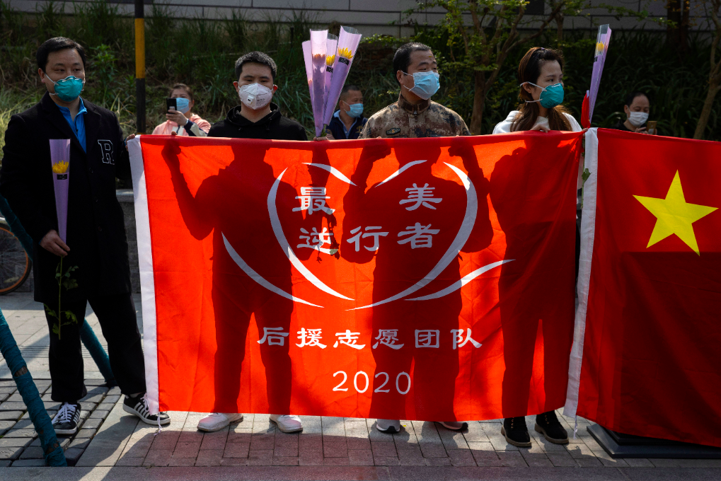 中國湖北民眾手舉旗幟悼念冠狀病毒中身亡的患者。 圖／美聯社
