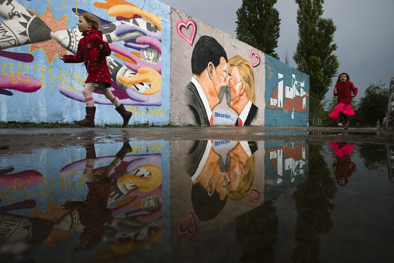 美中關係近來因疫情進一步惡化，圖為德國一名女童4月29日跑步經過柏林毛爾公園內的壁畫牆，牆上繪有美中領袖戴口罩親親的圖像。  美聯社