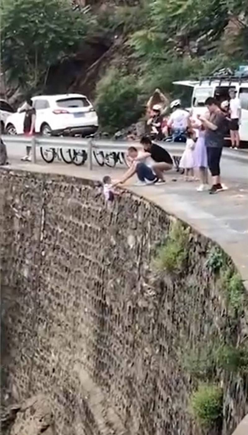 年約5歲的男童當日被一名男子捉着雙手吊在車道邊的懸崖外。圖／微博影片