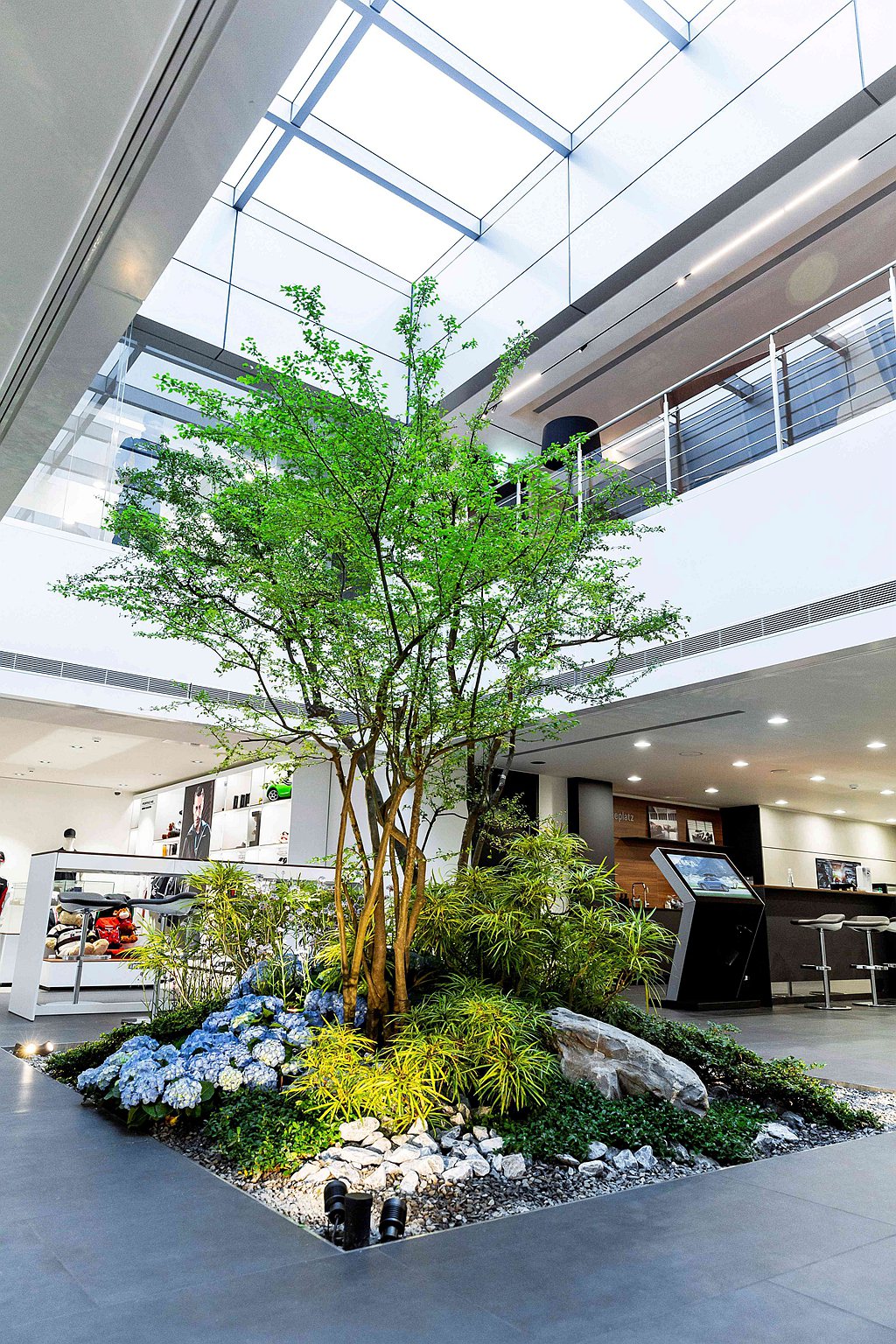 台北保時捷中心特別在室內打造天井融入一方綠意，以喬木、灌木、四季不同的花草，搭配...