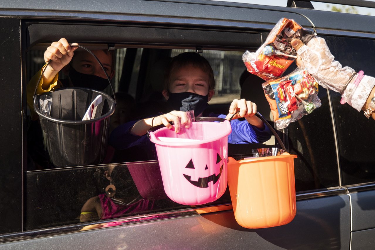 疫情之下，萬聖節（Halloween）的孩童傳統「不給糖就搗蛋」還是想維持。圖為美國加州蒙特利公園市一位家長，讓孩子戴上口罩在自家車內，以「得來速」方式，跟鄰居要來糖果。歐新社